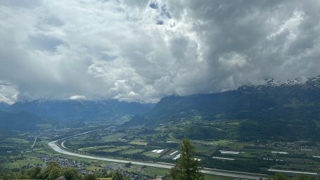 Rheintal Berglandschaft mit Wolken und Fluss im Tal, umgeben von grünen Wiesen.